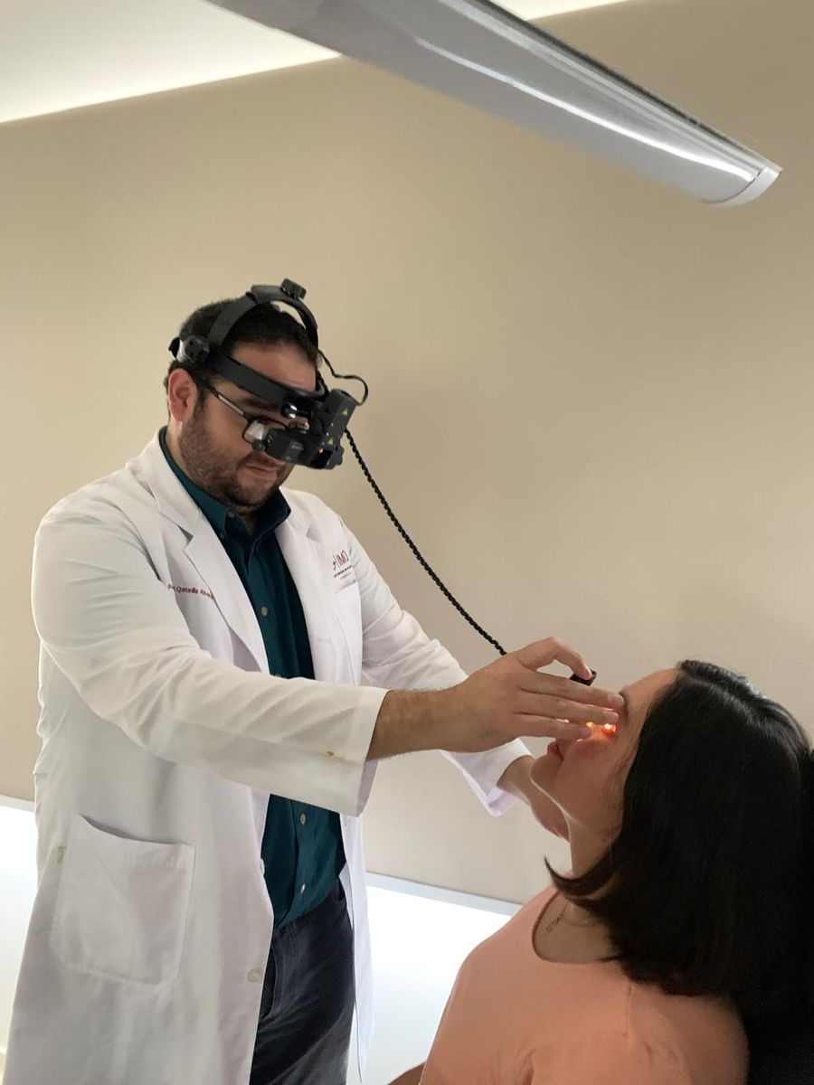 El doctor realizando una exploración de fondo de ojo a una paciente con oftalmoscopio indirecto de casco
