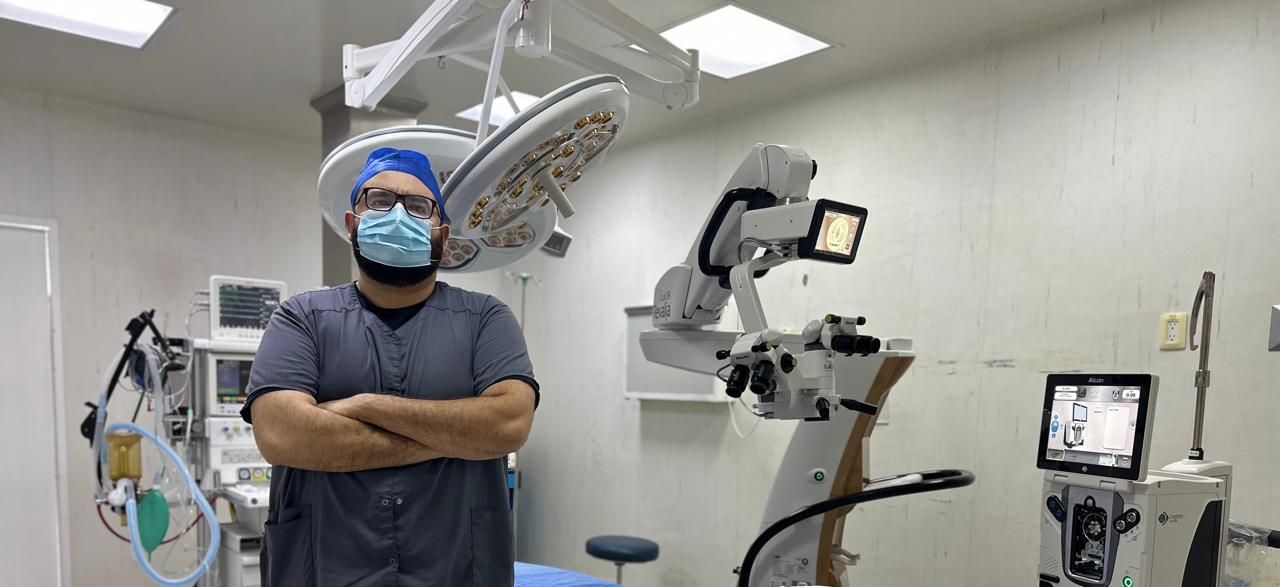 El Dr. Aubert Quintanilla en el quirófano oftalmológico, con el microscopio quirúrgico y el equipo de facoemulsificación al fondo